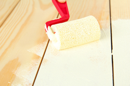 Paint roller brush with white paint, on wooden background